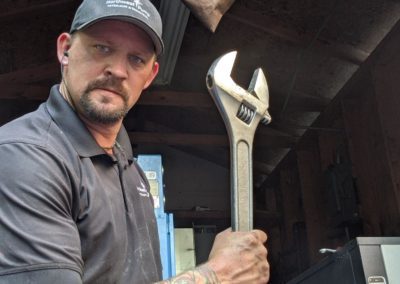 Photo of a technician with an arm tattoo holding a large adjustable wrench